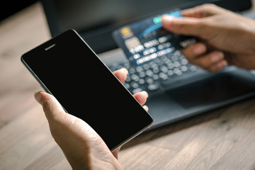 Hand holding smart phone and credit card for shopping online with laptop