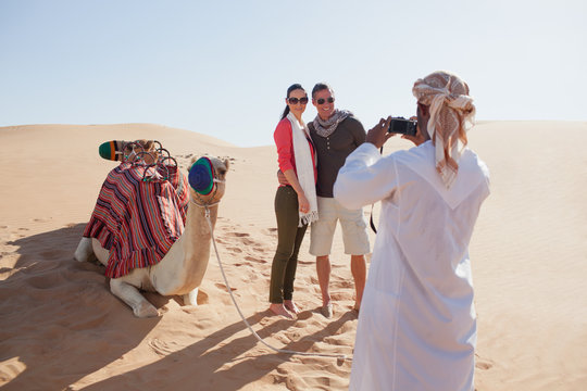 Arab man photographing couple at desert.