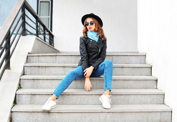 Fashion woman model wearing black rock jacket, hat posing in city