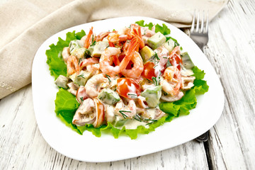 Salad with shrimp and avocado in white plate on light board