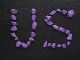 Letter US made out of purple rocks on a dark background.