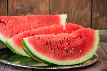 Slices of watermelon on a metal dish on a wooden background. Rustic style.