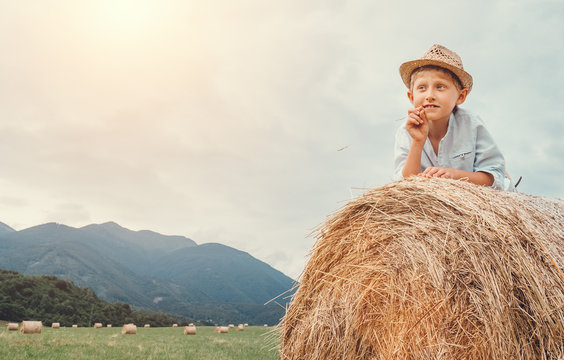 Boy in sraw hat lying on hay roll
