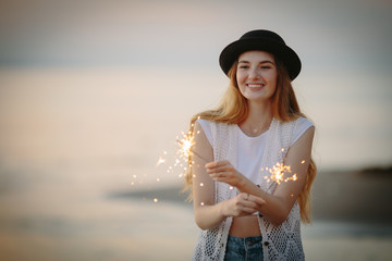 Teenage beautiful girl with sparklers on the beach at sunset