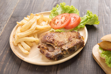 grilled pork chop steak and vegetables with french fries on wooden background