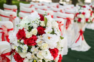 Wedding ceremony outdoors. White chairs with red ribbon.