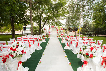 Wedding ceremony outdoors. Wedding arch decorated with red flowers.