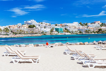 Sunbeds and beautiful city view on a beautiful beach in Ibiza, Spain.