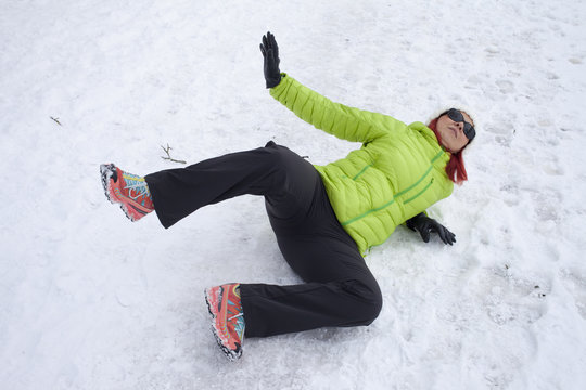 Risk Of Accidents In Winter. Mid Aged Woman Is Slipping And Falling On Footpath, Street Covered With Snow And Black Ice