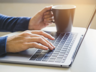 Woman hand type on Laptop Keyboard with Coffee cup Morning light