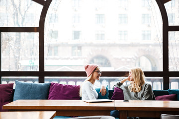 Two smiling women talking at the table in cafe