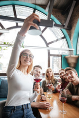 Happy friends sitting in cafe and make selfie by phone.