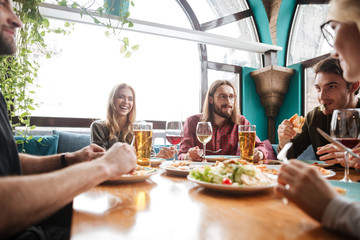 Young attractive friends sitting in cafe eating pizza