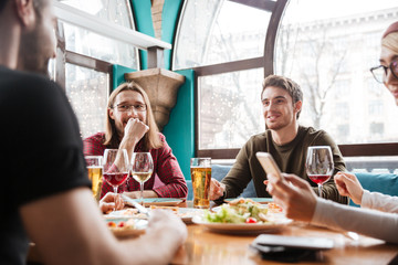 Happy friends sitting in cafe eating and drinking alcohol