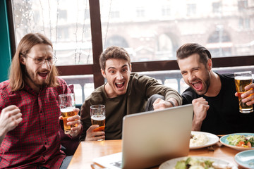 Happy men friends sitting in cafe eating and drinking beer