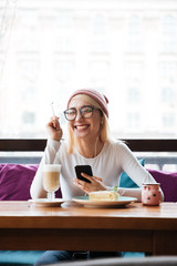 Cheerful young woman using mobile phone and laughing in cafe