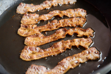 Bacon slice being cooked in frying pan.