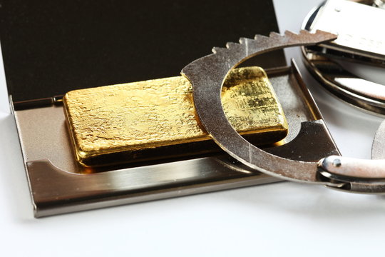The gold bar put in the metal name card box and chrome metal handcuffed  represent the crime and business with finance concept related idea.