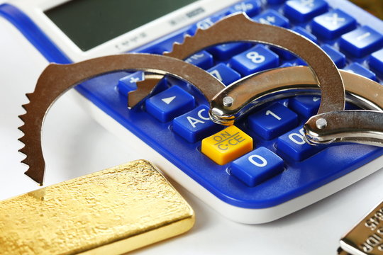 The chrome metal handcuffed put on the old blue color calculator in the scene appear gold bar also represent the crime and business with finance concept related idea.
