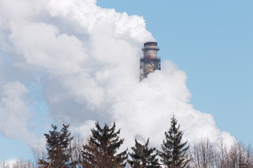 factory chimney, wrapped in white smoke against a blue winter sky