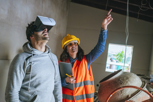 Woman on construction site showing a man with virtual reality glasses the house