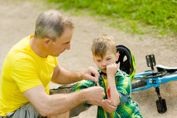 Grandfather putting band-aid on young boy's injury who fell off his bicycle