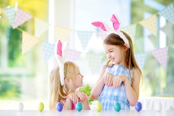 Two cute little sisters wearing bunny ears playing egg hunt on Easter