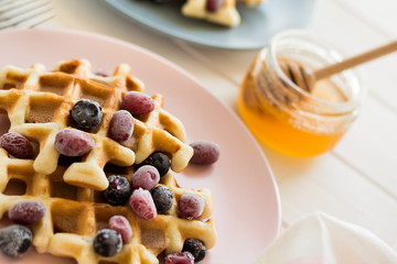Belgian waffles with honey and frozen berries on white wooden table. Selective focus