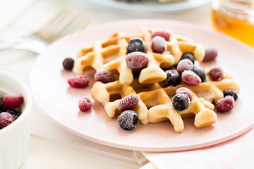 Belgian waffles with honey and frozen berries on white wooden table. Selective focus
