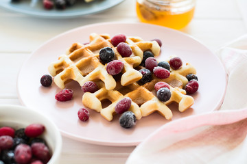 Belgian waffles with honey and frozen berries on white wooden table. Selective focus