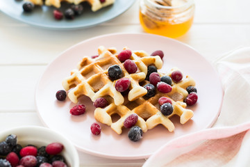 Belgian waffles with honey and frozen berries on white wooden table. Selective focus