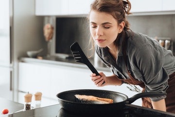 Beautiful lady standing in kitchen while cooking fish