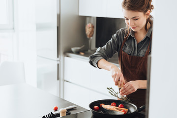 Happy lady standing in kitchen while cooking fish