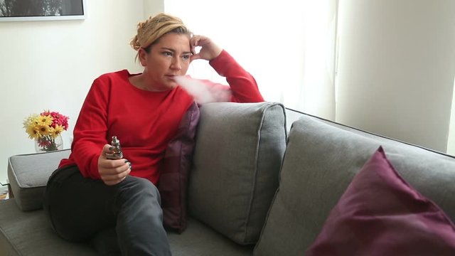 Relaxed Middle Aged  Woman Lying On A Sofa Smoking Using E- Cigarette
