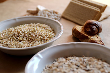 Oats and rice in a bowl close-up. Rice cakes and bread in background.