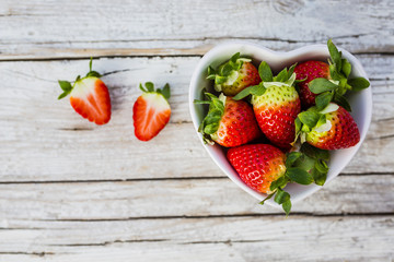 Fresh and ripe strawberries in a bowl in the shape of heart on wooden background.