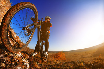 Fototapeta na wymiar Man on mountain bike on the background of beautiful sunset. Bicycle wheel closeup.
