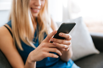 Beautiful young woman sitting and using cell phone at home