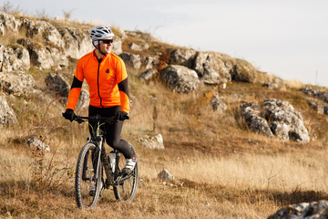 Cyclist in Orange Jacket Riding the Bike on the Rocky Trail. Extreme Sport Concept. Space for Text.