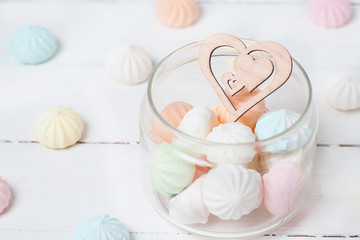 Color zephyrs and wooden figure of heart in glass jar on white wooden table. Concept of St. Valentine's Day