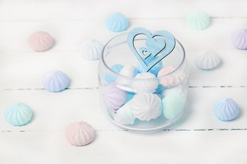 Color zephyrs and wooden figure of heart in glass jar on white wooden table. Concept of St. Valentine's Day