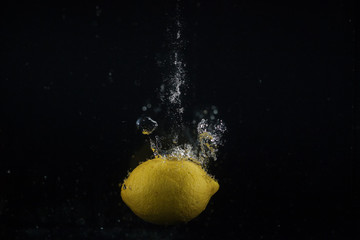 Fototapeta na wymiar Juicy lemon sinks in water on black background