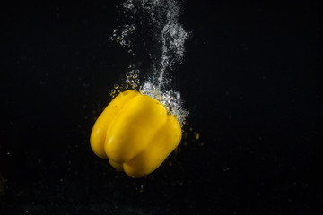 Bubbles surround yellow pepper while it sinks on black background