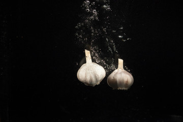 Two pieces of garlic fall in water on black background