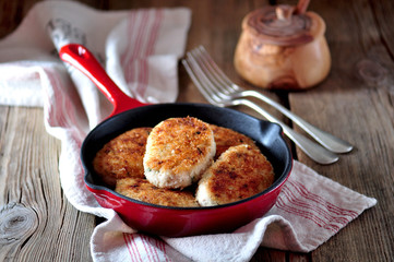 Chicken cutlets( burgers) in a cast iron skillet over an old wooden background.