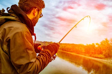 Deurstickers Jonge man vissen op een rivier vanaf de boot bij zonsondergang © zeljkomatic76