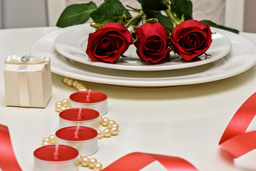 Red Roses on a white plate, candles and giftbox. Romantic composition for Valentine's Day, Anniversary, Events. Place for text