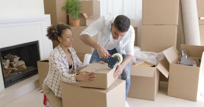 Young couple packing boxes to move home working as a team to tape up full cartons on the living room floor