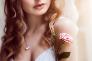 Obraz na płótnie Canvas Tender pink rose touches woman's shoulder while she poses in white lingerie