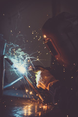 Metalwork industry background of man welding loops of steel pipe, generating sparks, smoke and reflexions - obrazy, fototapety, plakaty